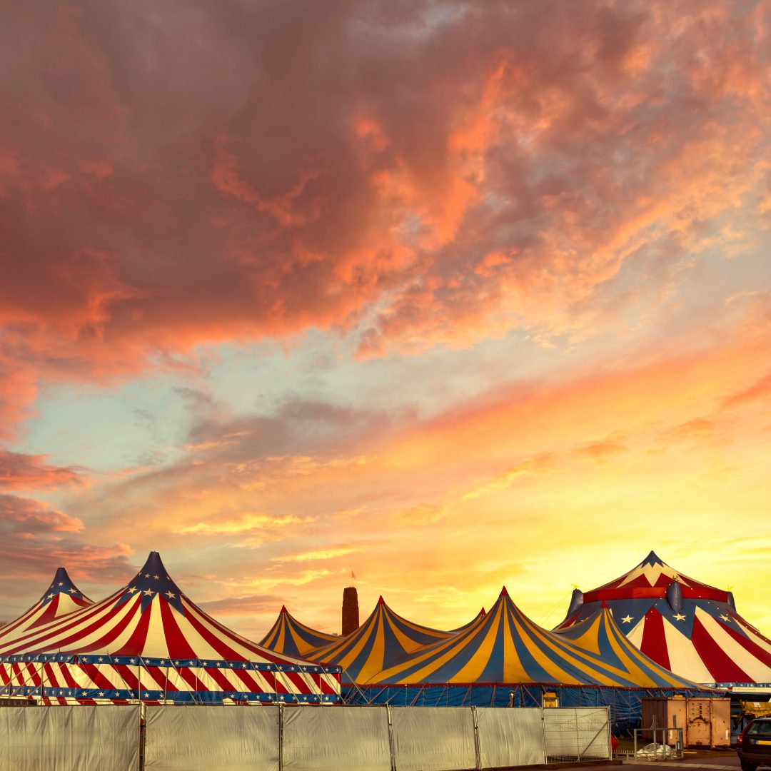 Red and white circus tents topped with bleu starred cover against a sunny blue sky with clouds