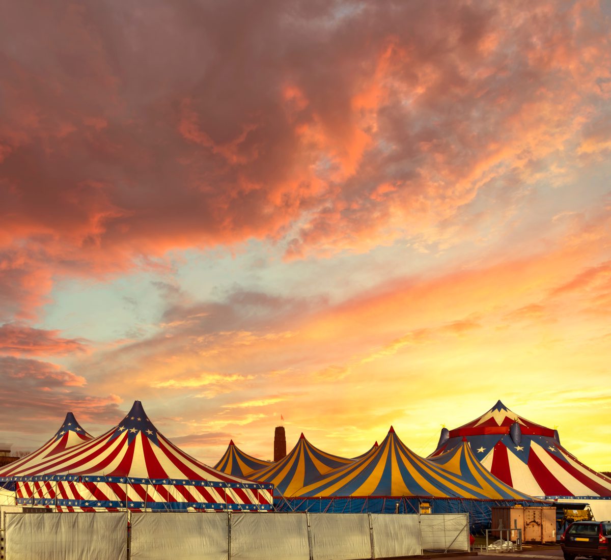 Red and white circus tents topped with bleu starred cover against a sunny blue sky with clouds